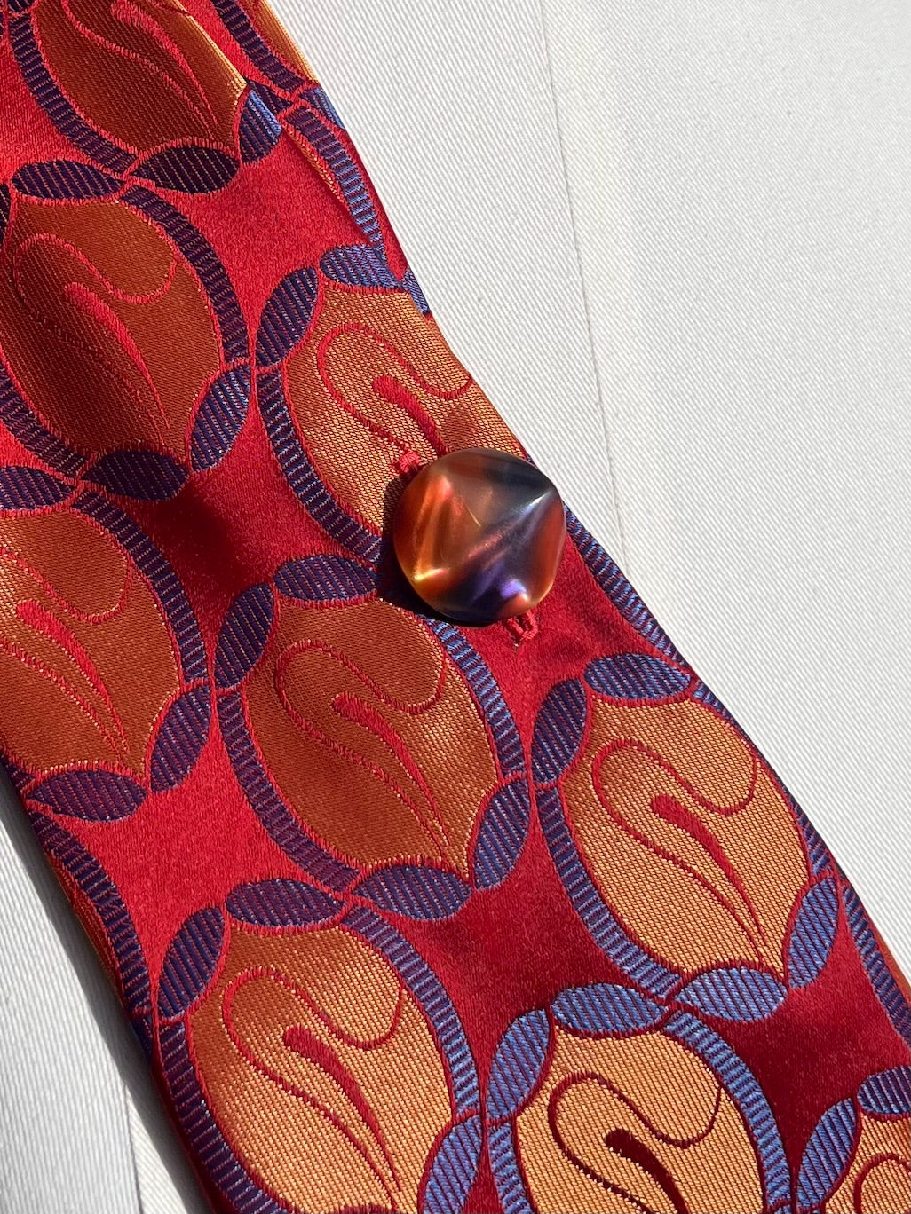 Detail: alter italienischer Knopf, marmoriert in Orange und Violett, auf rotem Jacquard