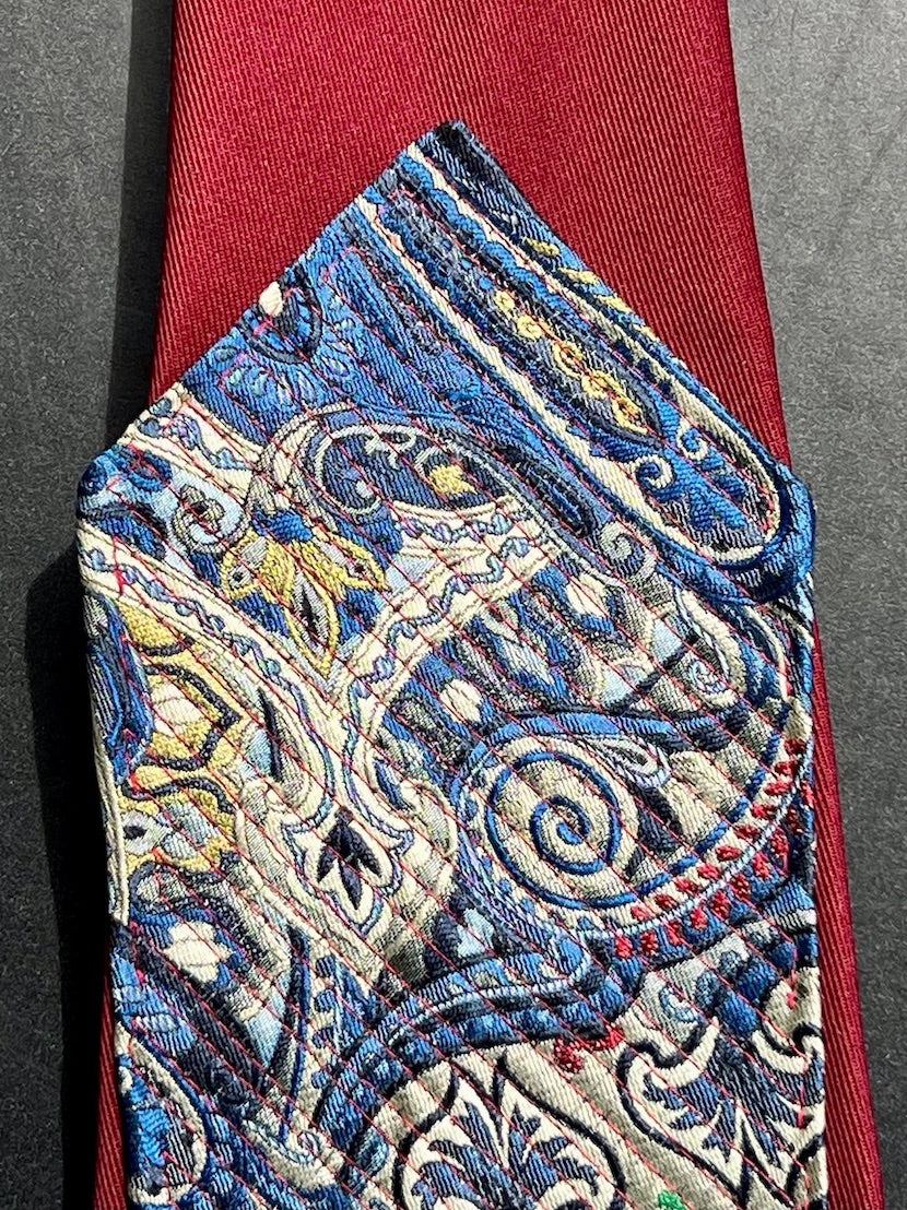 Detail: rote Steppnähte auf blauem Paisley neben bordeauxfarbenem Krawattenstoff