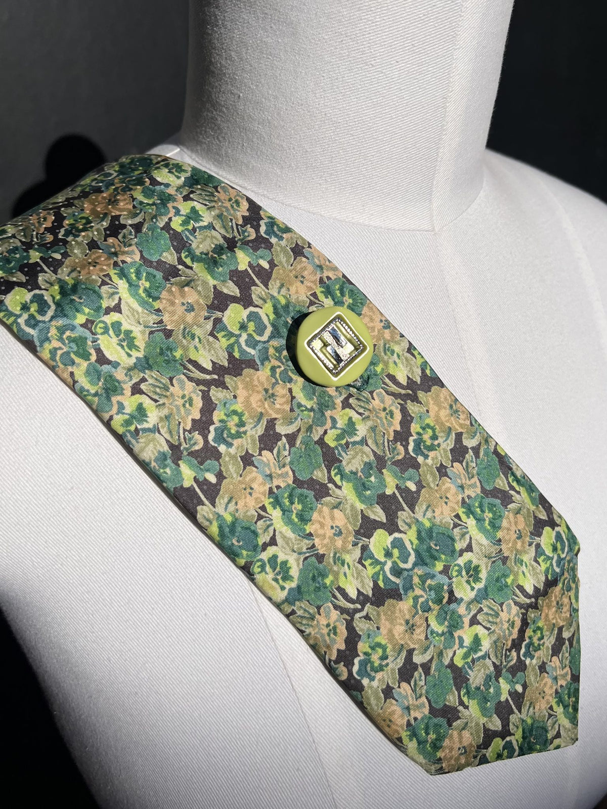 Detail: hellgrüner Vintage-Knopf mit silbernem Einsatz auf grünem Blumenmuster