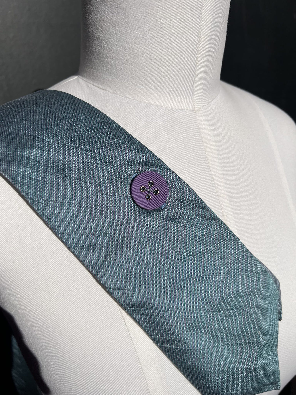 Detail: lila Stoffknopf auf graublauem Krawattenstoff