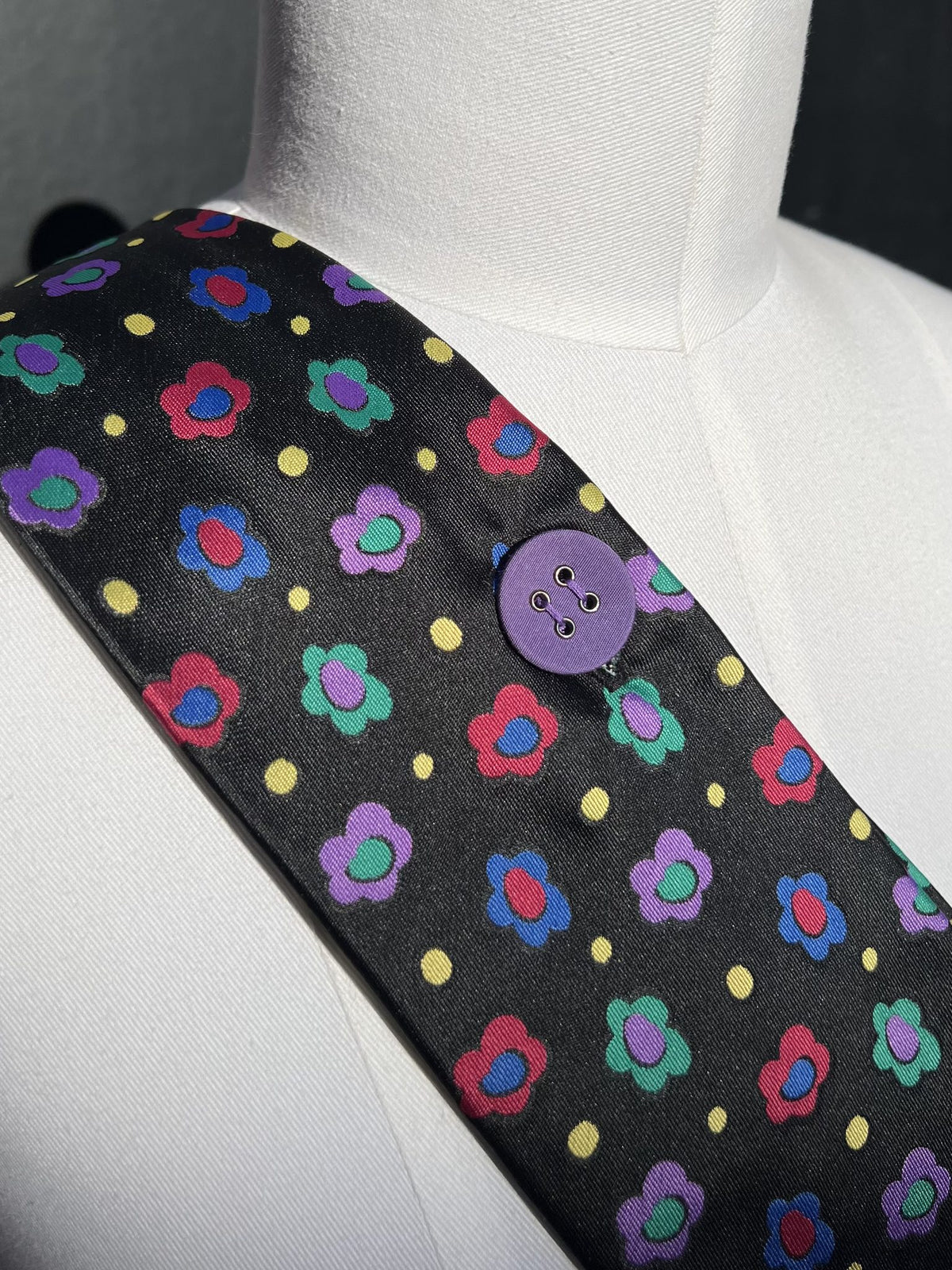Detail: lila Knopf auf schwarzem Stoff mit pinken, blauen und grünen Blüten