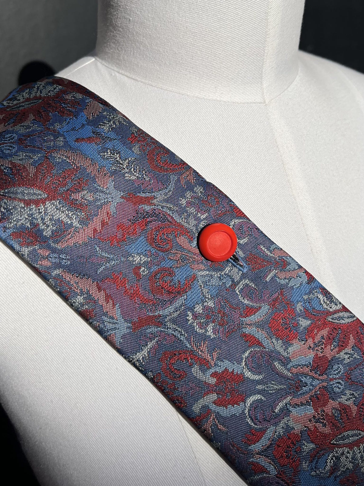 Detail: roter Knopf auf blauem Stoff mit rotem Paisley